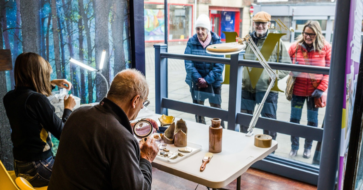 Group of people looking in window at Open Lab as people work with artefacts found at Bishop Auckland.